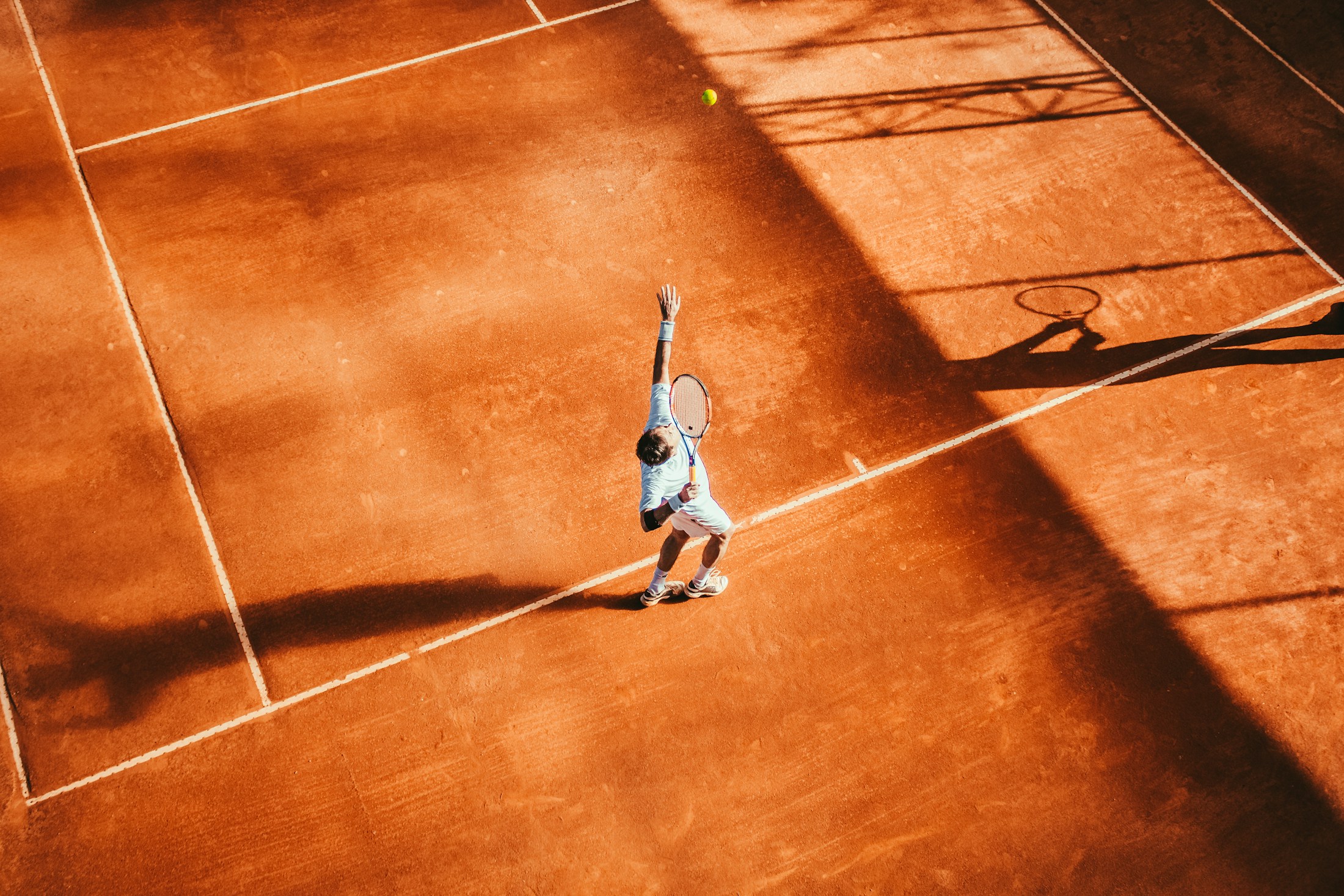 Overhead view of a tennis player serving on an orange clay court